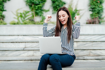 happy and excited woman sitting with laptop outdoors