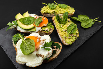 Sandwiches with avocado, spinach and fried eggs on a black background