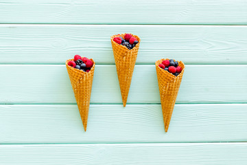 Fresh berries in waffle cones on mint green wooden background top view