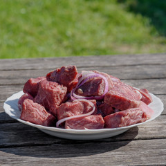 Raw fresh beef meat slices in a white bowl with onion  on the wooden table in the yard of countryside house.