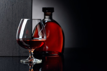 Glass and bottle of brandy on a black reflective background.