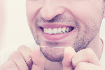 Man looks in the mirror, smiling, he uses dental floss, man's hands, close up, toned