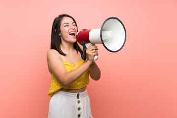 Young Mexican woman over isolated wall shouting through a megaphone