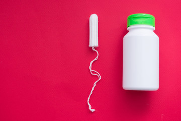 Tampon and white container of medicine on a red background, top view, close up