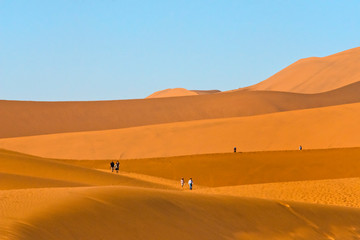 Fototapeta na wymiar Tourists hiking on red sand dune in southern Namib Desert, Sossusvlei, Namib-Naukluft National Park. Hardap Region, Namibia.