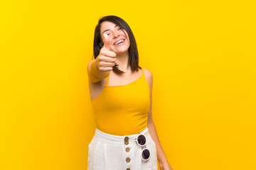 Young Mexican woman over isolated yellow background with thumbs up because something good has happened