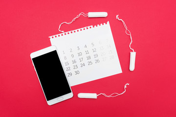 Fototapeta na wymiar Tampon, calendar and white smartphone, red background, copy space, advertising, close up, top view