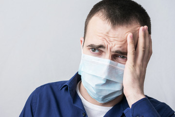 Young man in a medical mask, he has a headache, squeezes his head with his hands, close up, portrait, health care concept