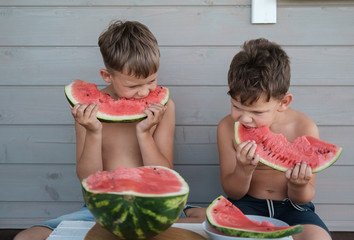 two brothers eat a ripe juicy watermelon on the veranda of the house on a warm summer day. boys eat...