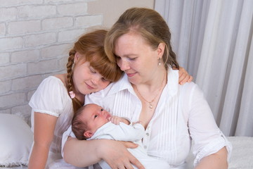 Little red-haired girl with mom in a white dress leaned over with a newborn baby