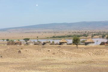 Fototapeta premium Landscape near Arusha, Tanzania, native oval grass huts stand in front of a long lake, with a full moon overhead.