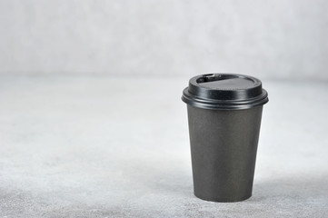 Paper cup with coffee. The paper cup is black, the lid is black plastic. The concept of fast food and coffee to go. Light background. Free space for text.