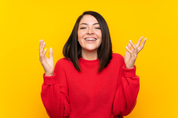 Young Mexican woman with red sweater over yellow wall laughing