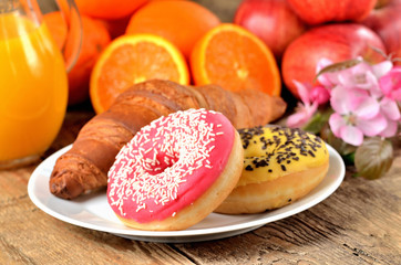 Donuts, croissant, orange juice and spring flowers on wooden table