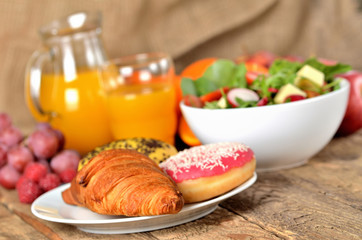 Detail of croissant and donuts, orange juice and fresh salad - breakfast on wooden table