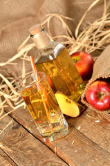 Juice from fresh apples, straw, ice and bottle in background on wooden table vertical photo