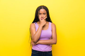 African American teenager girl with long braided hair over isolated yellow wall thinking