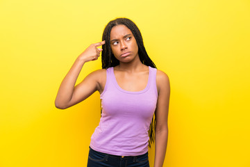 African American teenager girl with long braided hair over isolated yellow wall making the gesture...