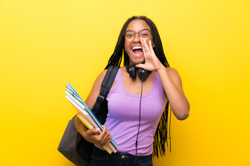 African American teenager student girl with long braided hair over isolated yellow wall shouting...