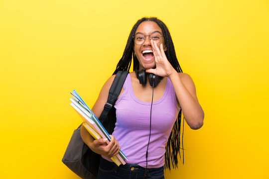 African American Teenager Student Girl With Long Braided Hair Over Isolated Yellow Wall Shouting With Mouth Wide Open