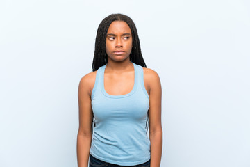 African American teenager girl with long braided hair over isolated blue background standing and looking to the side