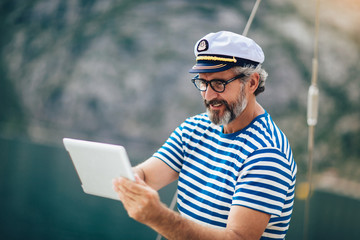 Mature man standing on the deck of his boat and using digital tablet on a sunny afternoon.