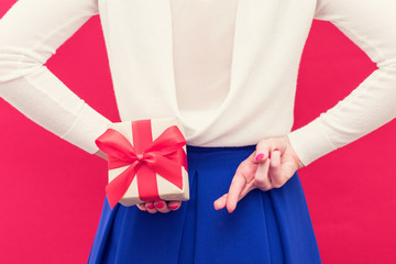Woman holding a gift box behind her back, fingers crossed behind her back, front view, close up