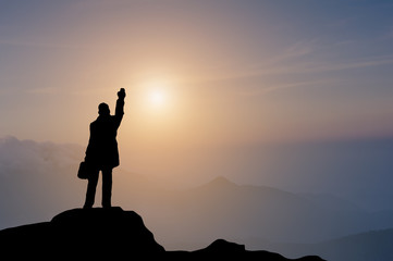 Selective focus silhouette miniature business man holding briefcase and push the hand up standing on top of mountain with sun raise moment.  Success business business concept.