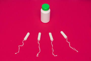 Tampons and white container of medicine on a red background, top view, close up