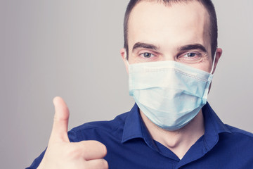 Attractive man in a medical mask smiles showing thumb up, portrait, close up, health care concept