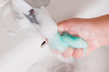 Maid holding sponge under running water. Bubbles forming in sink. Shiny and clean bathroom.