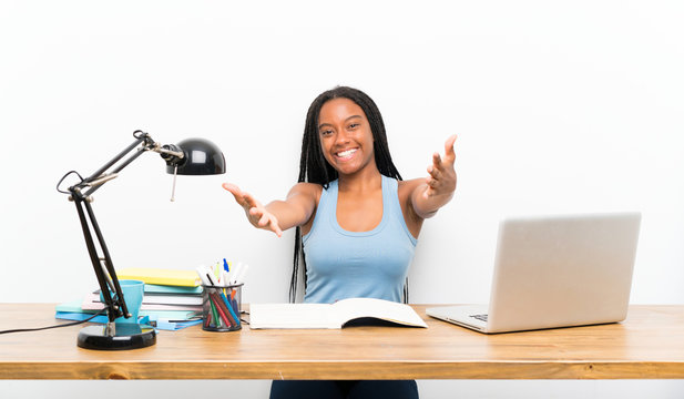 African American teenager student girl with long braided hair in her workplace presenting and inviting to come with hand