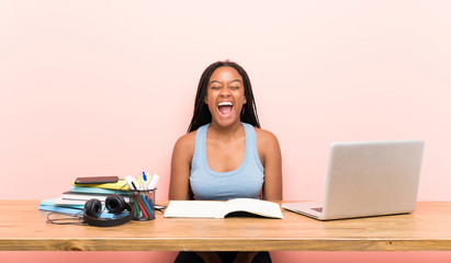 African American teenager student girl with long braided hair in her workplace shouting to the front with mouth wide open