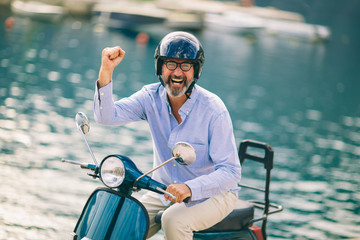 Mature man driving motor scooter in marina near the sea.