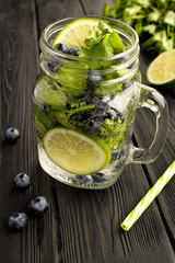 Infused or detox water with blueberries, cilantro and lime  on the  black  wooden  background. Location vertical. Closeup.
