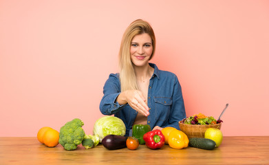 Young blonde woman with many vegetables shaking hands for closing a good deal