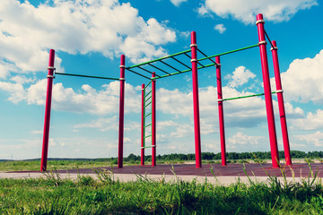 Fototapeta na wymiar Red horizontal bars against a blue cloudy sky in summer park