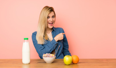 Young blonde woman with bowl of cereals pointing finger to the side