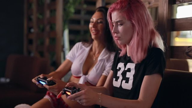 Two sexy unconventional girls playing the tv video game holding joysticks