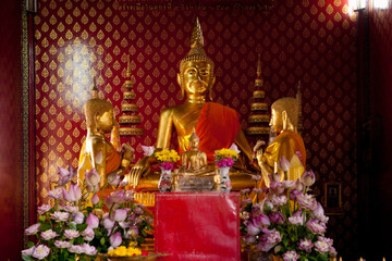 Bangkok, Thailand - Three gold-colored statues pray amidst a flower arrangement in a Buddhist shrine.