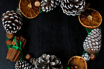 Christmas background with dry orange,white pinecone,green christmas tree balls,mandarins,red apple,ginger sticks,on a black background,flat lay,space for text,space for copy