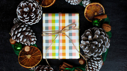 Christmas background with dry orange,white pinecone,green christmas tree balls,mandarins,red apple,ginger sticks,on a black background,flat lay,space for text,space for copy