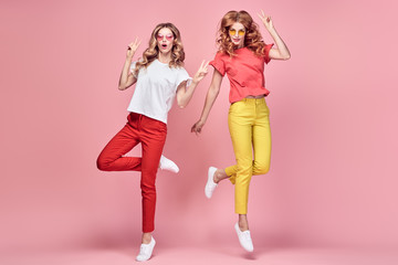 Two easy-going happy hipster Woman dance Fun, peace sign in Stylish fashion colored pants. Beautiful excited Girl in summer Trendy outfit, sneakers jump laughing. Creative dancing fashionable concept