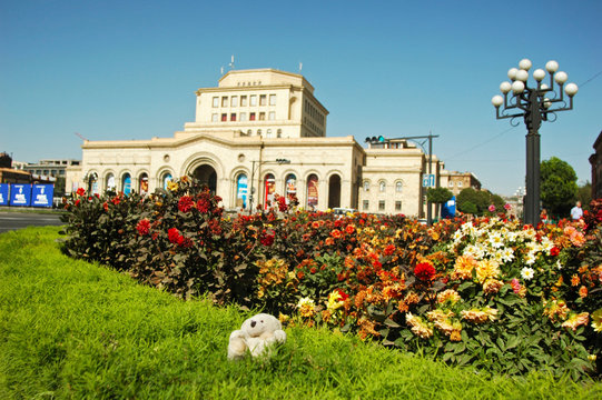 Armenia, Yerevan, stuffed toy Boris on the grass with an old white building in the background on Hanrapetutyan Hraparak (Republic Square)