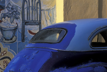 Cuba, Havana. Hand-painted blue car with several hues in front of wall mural.