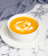 Two bowls of pumpkin soup on white background with gray fabric and slices of butternut squash,top view,vegetarian food