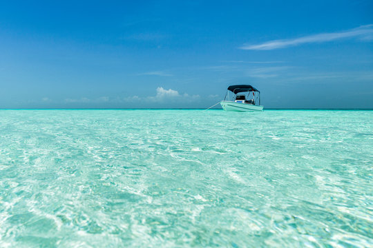 A boat is anchored over a shallow sandbar in clear waters near Staniel Cay, Exuma, Bahamas