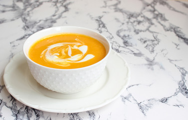 Two bowls of pumpkin soup on white background with gray fabric and slices of butternut squash,top view,vegetarian food