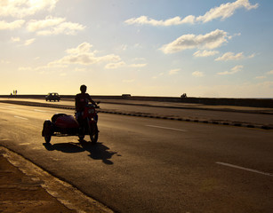 Havana, Cuba, silhouetted person traveling along the Malecon highway on a motorbike along the seawall