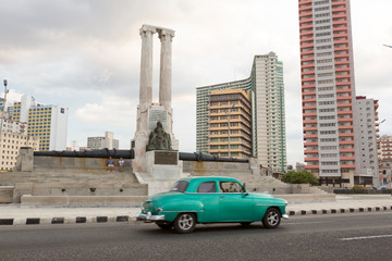 Cuba, Havana. Vintage car passes monument.